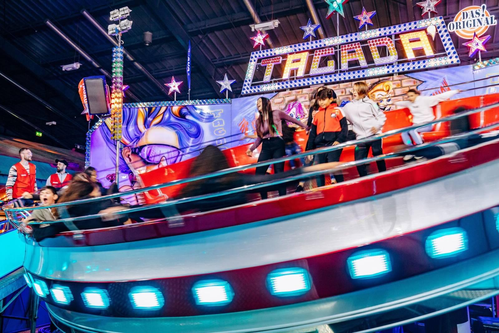Des jeunes riant et criant sur la « Tagada », la tasse qui tremble, dans le hall d'exposition.